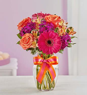 Bouquet of pink and orange flowers in a clear glass vase with a ribbon