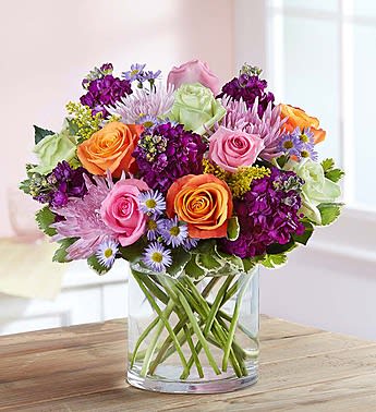 Colorful bouquet of roses and purple flowers in a clear glass vase