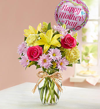 Bouquet of pink roses and yellow lilies in a glass vase with a Mother's Day balloon