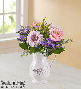 Pink and purple flowers arranged in a white pitcher vase