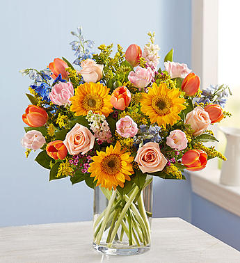 Colorful bouquet of tulips, roses, and sunflowers in a clear glass vase