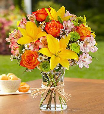 Bouquet of yellow lilies, orange roses, and pink alstroemeria in a glass vase