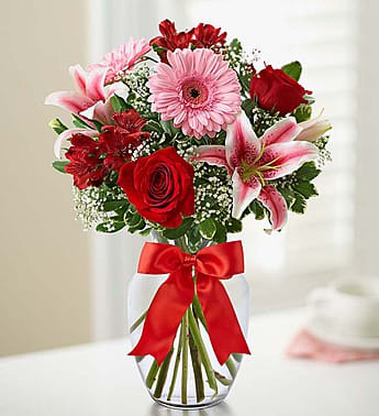 Bouquet of red and pink flowers in a clear glass vase with a red ribbon