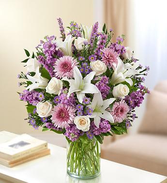 Bouquet of white lilies, pink daisies, and purple flowers in a glass vase