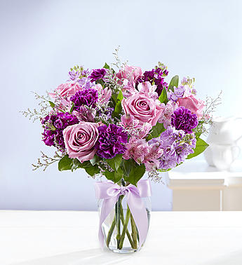 Pink and purple bouquet in a clear glass vase with a lavender ribbon