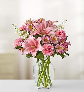 Pink lilies and carnations arranged in a clear glass vase