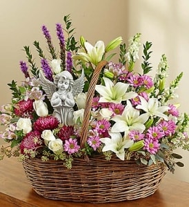 Basket arrangement of white lilies, pink flowers, and a small angel figurine
