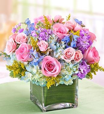 Pink roses and purple flowers arranged in a square glass vase