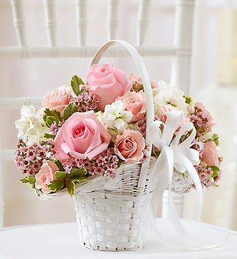 Pink roses and white flowers arranged in a white basket with a ribbon