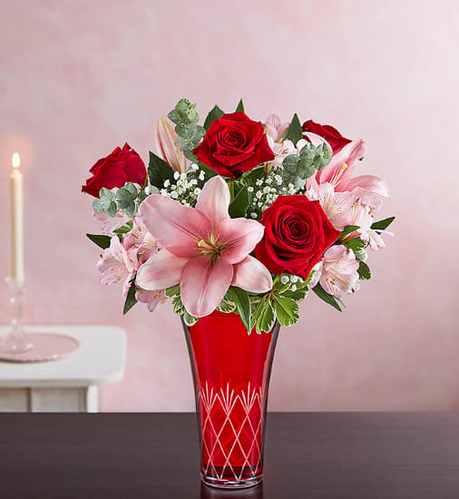 Red roses and pink lilies arranged in a red glass vase