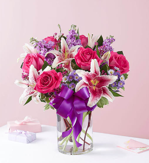 Pink roses and lilies in a glass vase with a purple ribbon