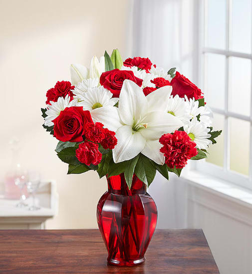 Red roses, white lilies, and daisies in a red glass vase