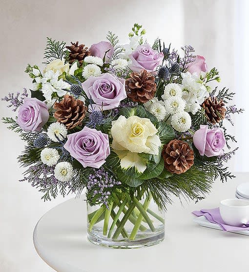 Lavender and white roses arranged in a clear glass vase with pinecones