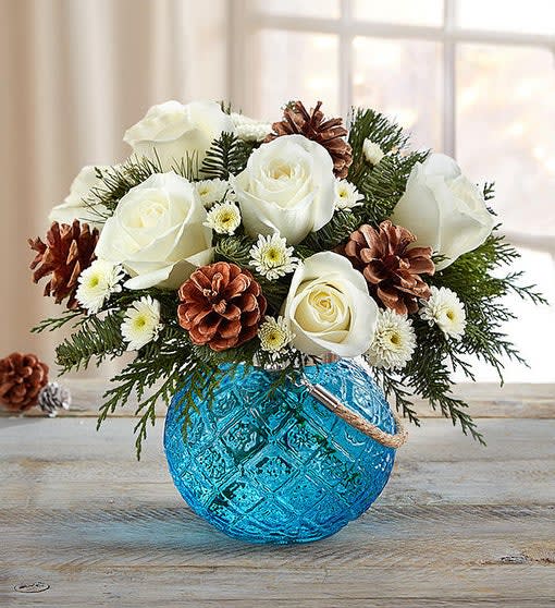 White roses and pinecones arranged in a blue glass vase