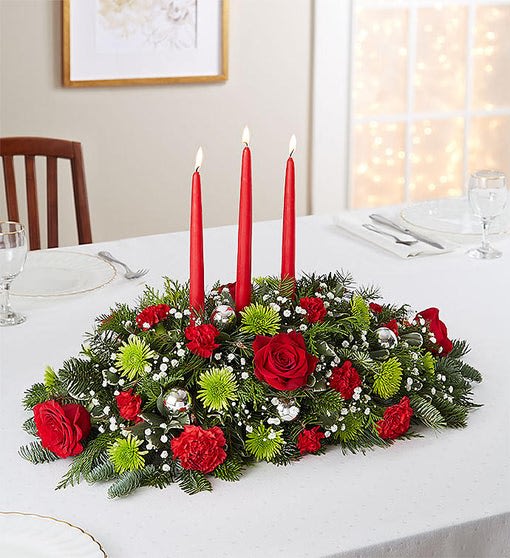 Red floral centerpiece with three tall red candles on a dining table