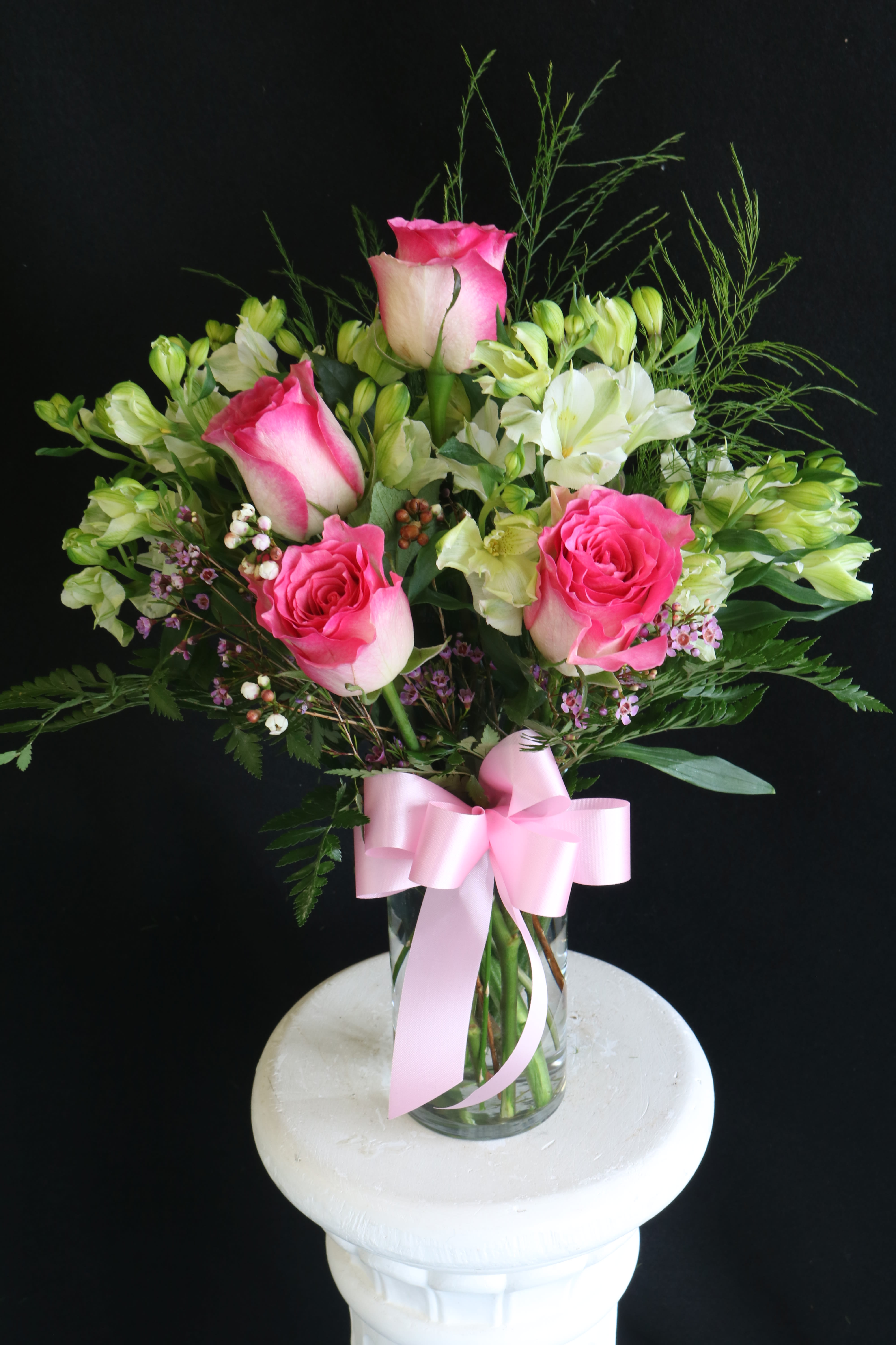 Pink roses and white alstroemeria in a glass vase with a pink ribbon