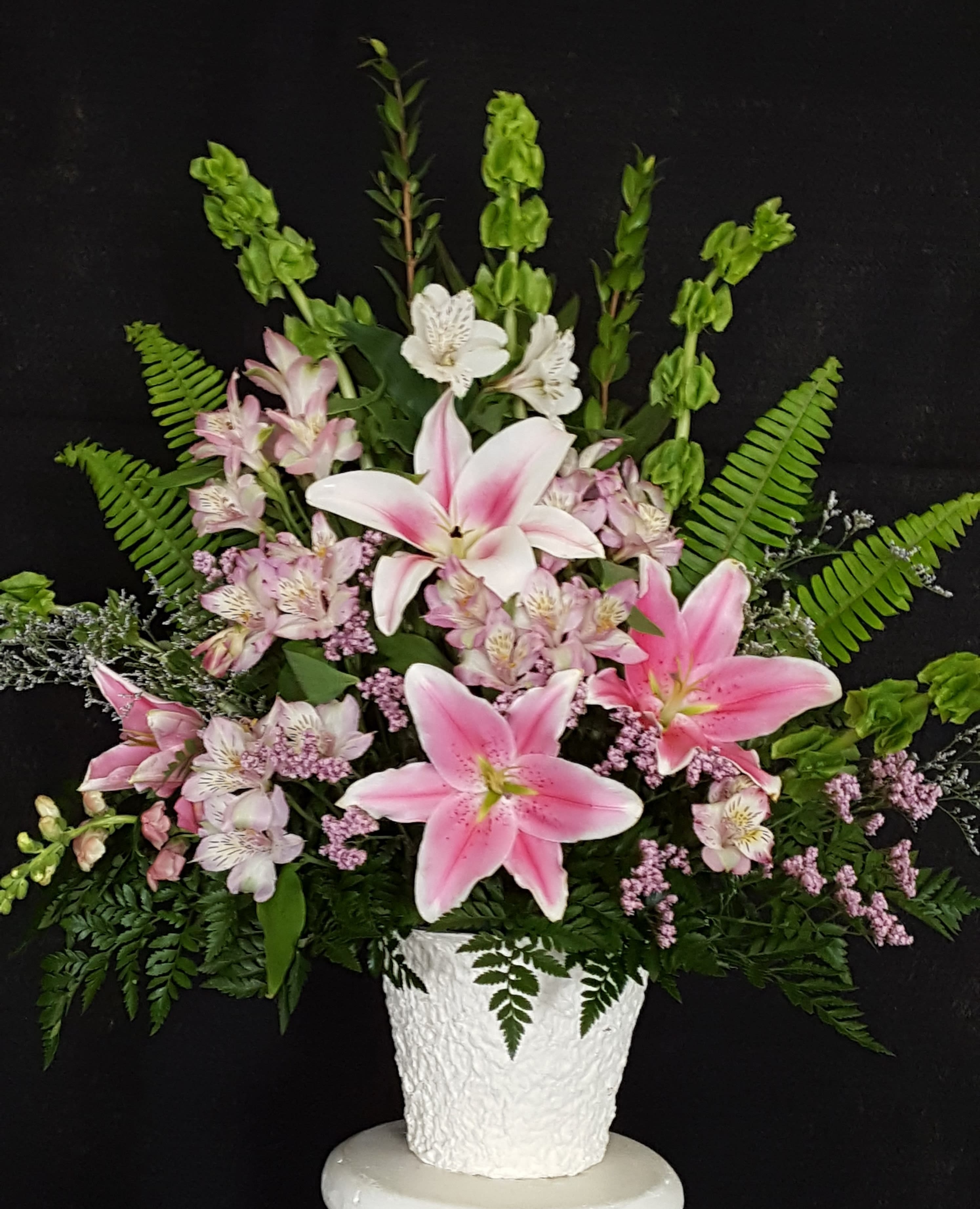 Pink lilies and small white flowers arranged in a white vase