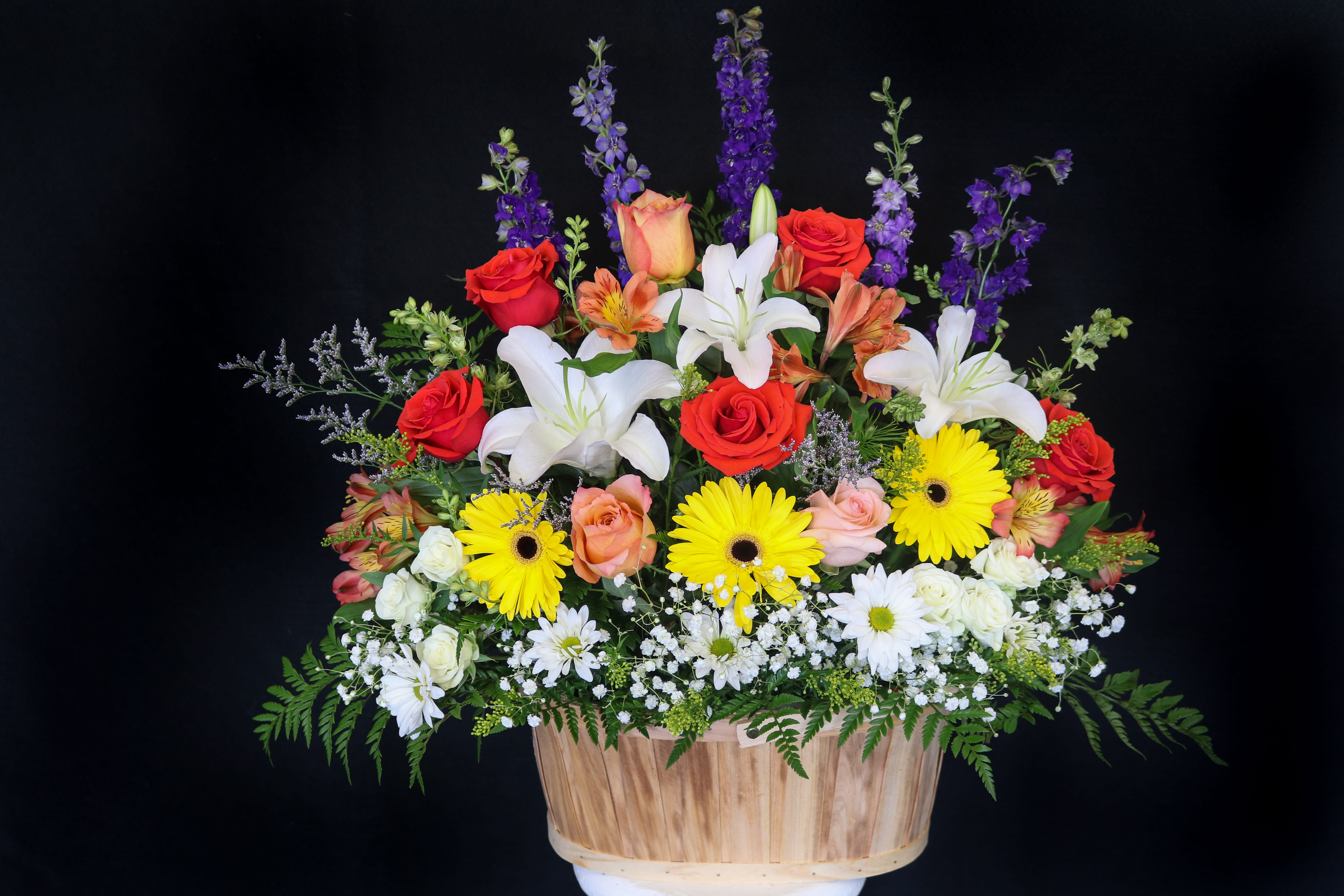 Mixed bouquet with roses, lilies, and daisies in a wooden basket