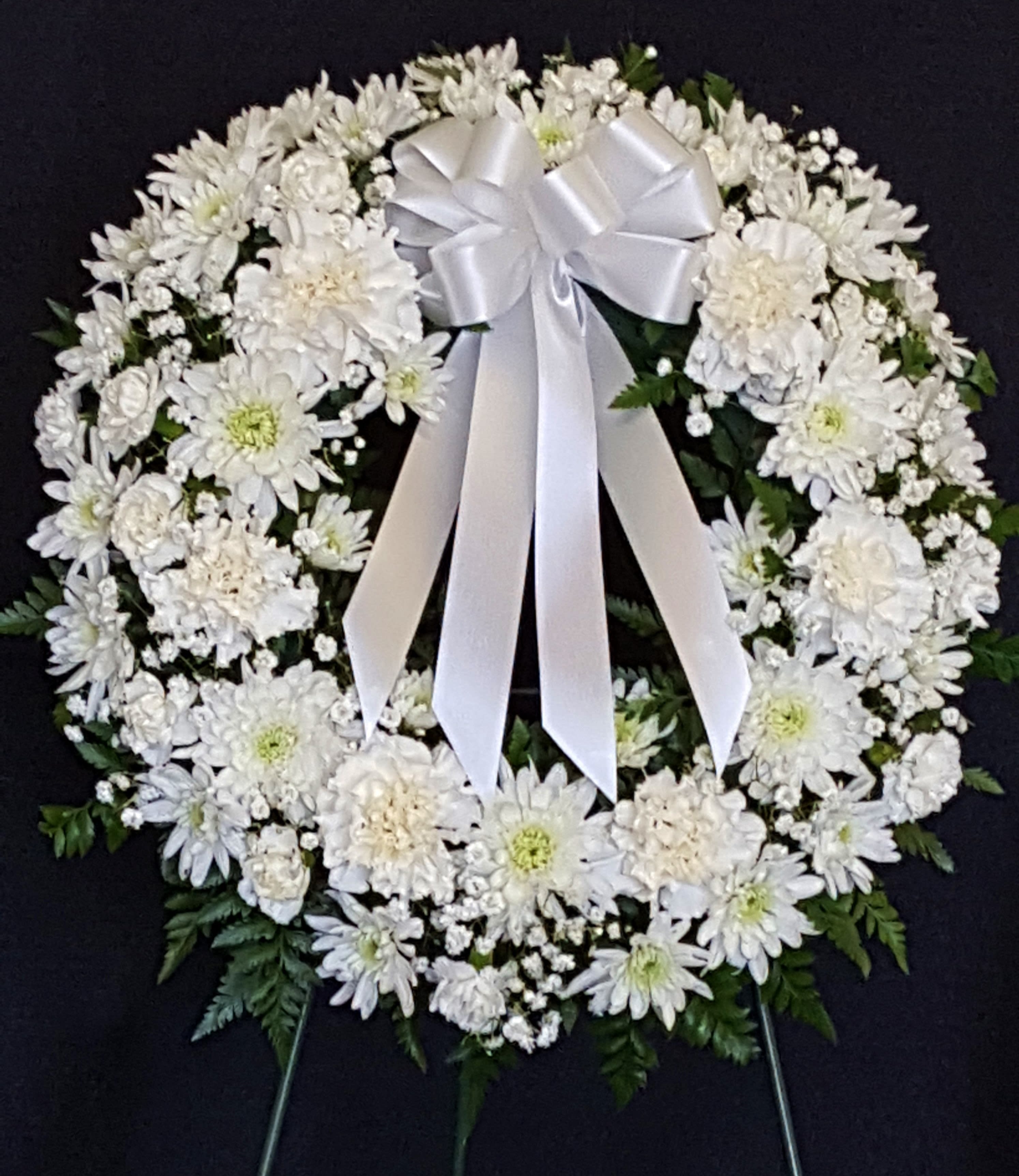 White floral funeral wreath with a satin bow on a dark background