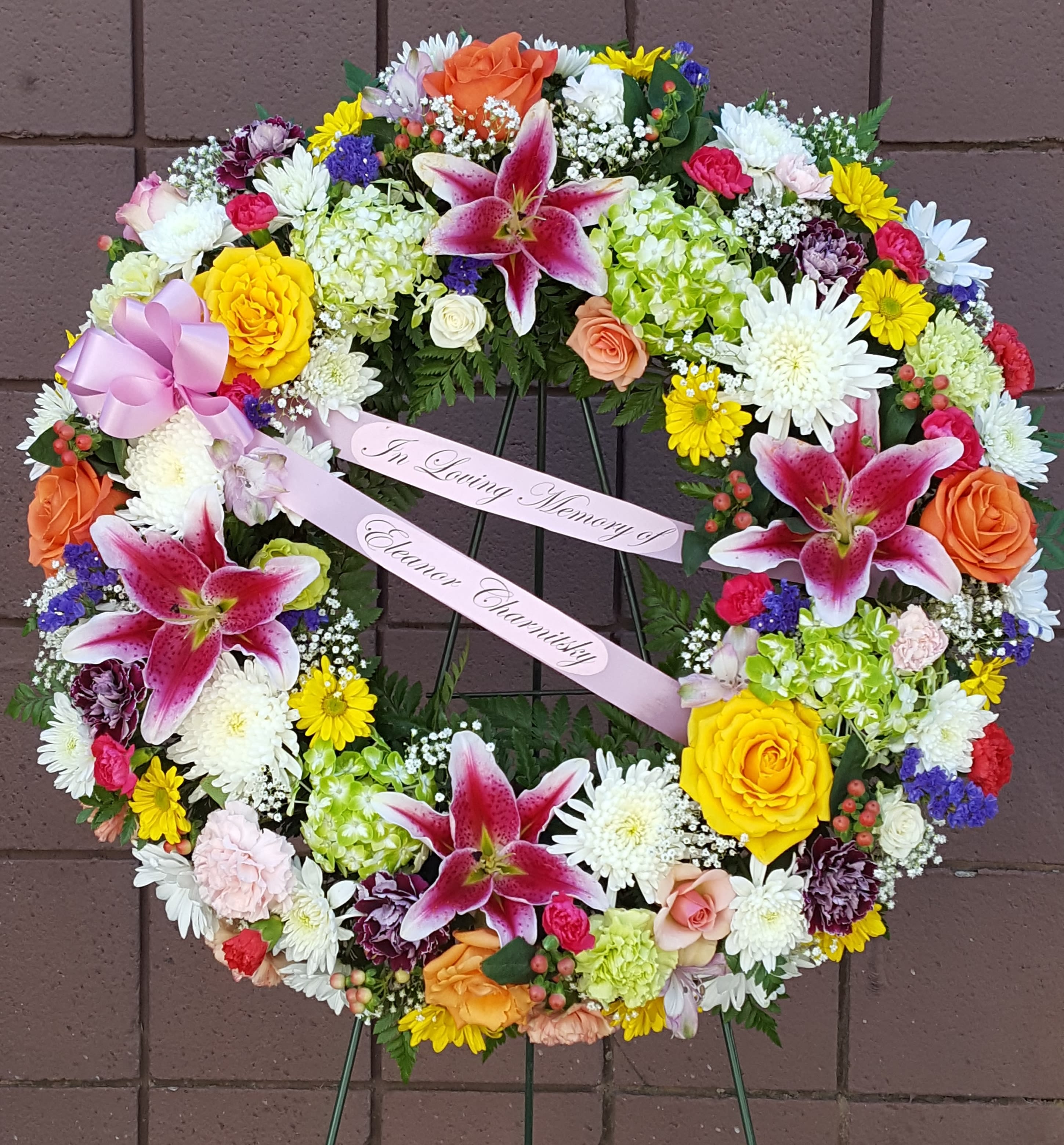Heart-shaped floral wreath with pink lilies and mixed blooms on a stand