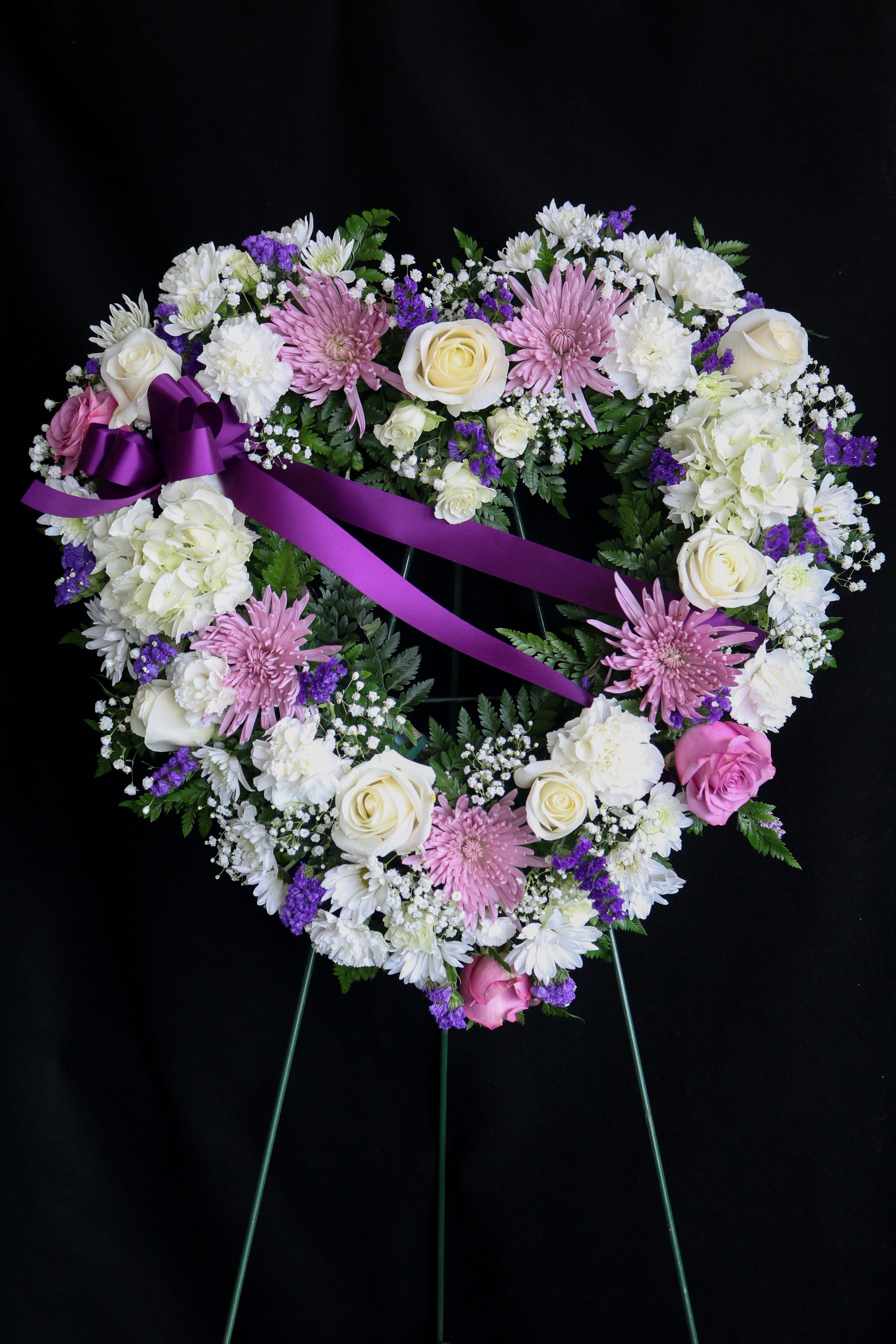 Heart-shaped floral wreath with pink and white flowers and a purple ribbon