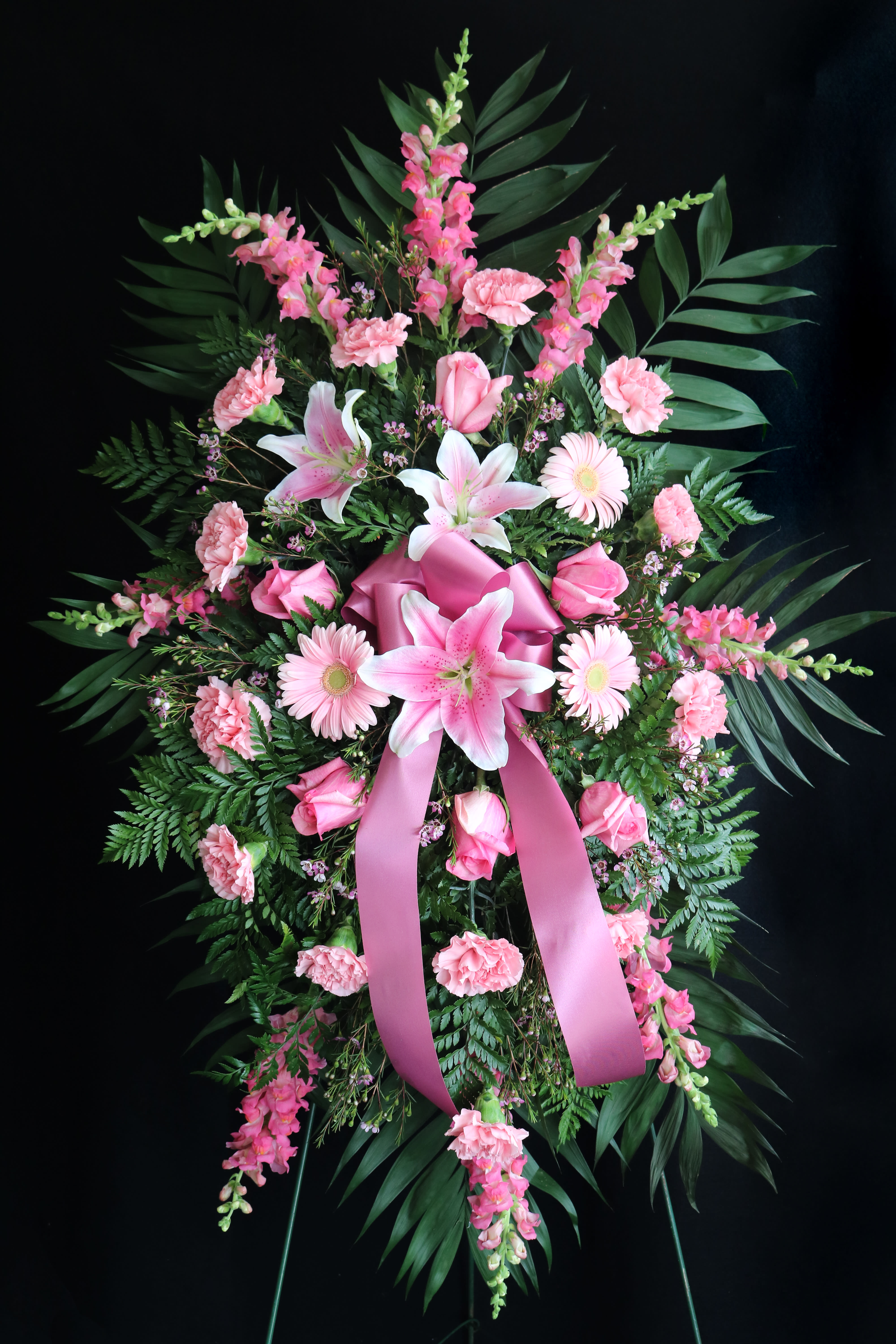 Pink floral standing spray with lilies, roses, and carnations on a ribboned easel