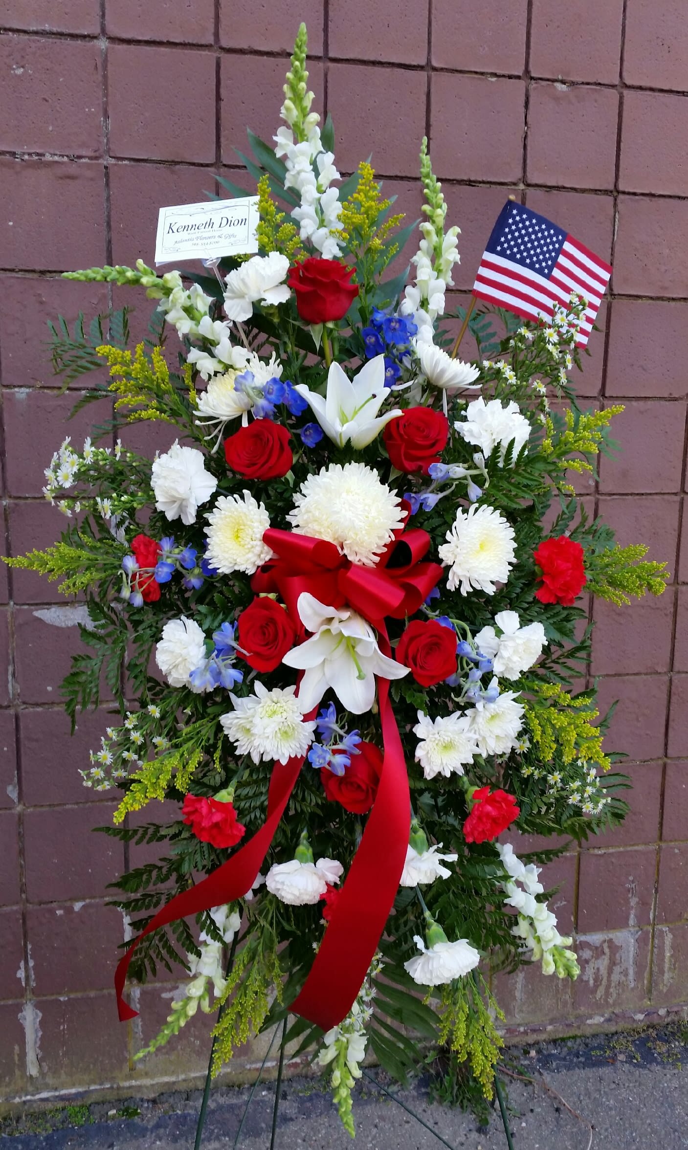 Standing floral spray with red roses, white lilies, and an American flag