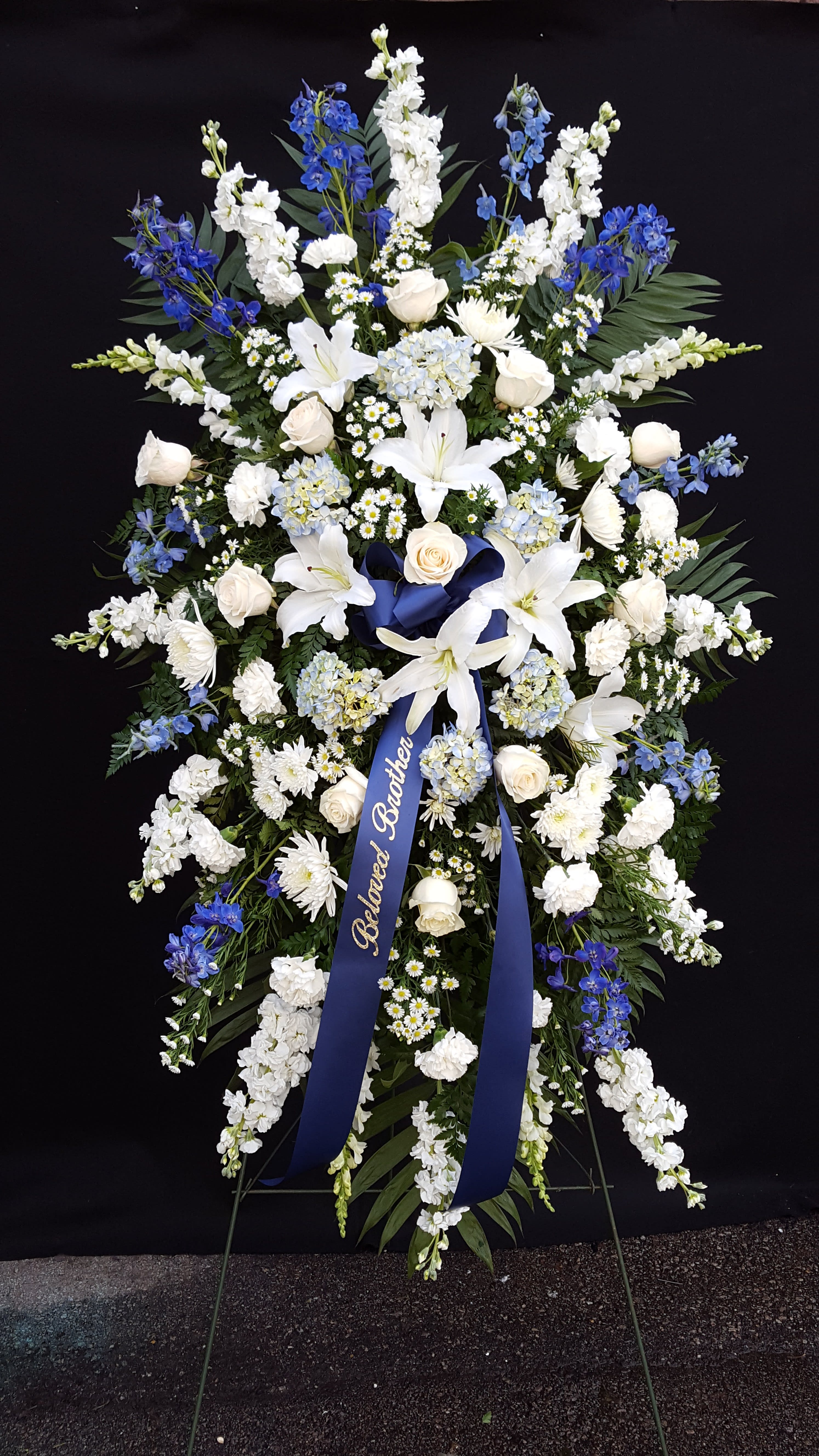 Large blue and white funeral spray with ribbon on an easel