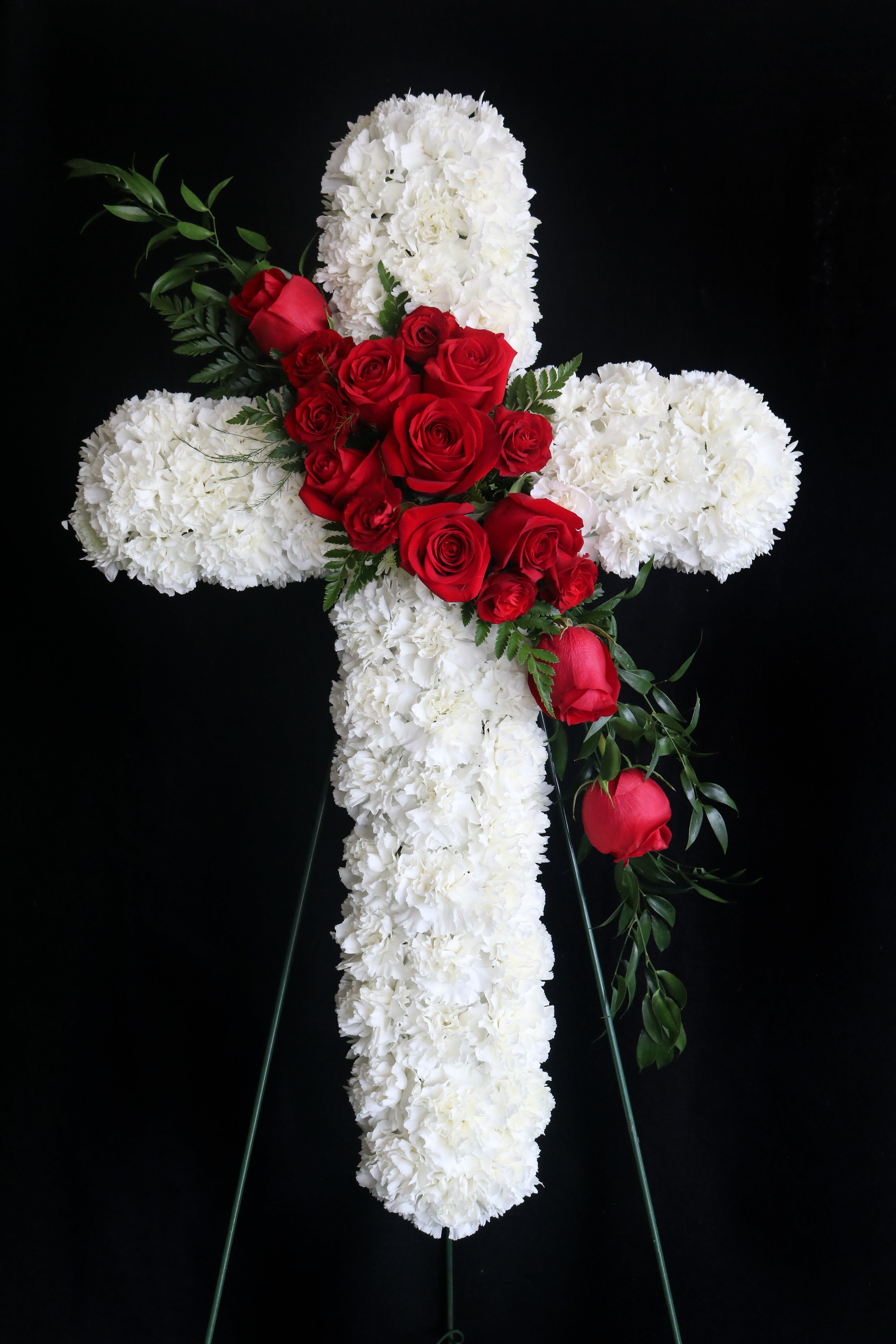 White floral cross with red roses on a black stand