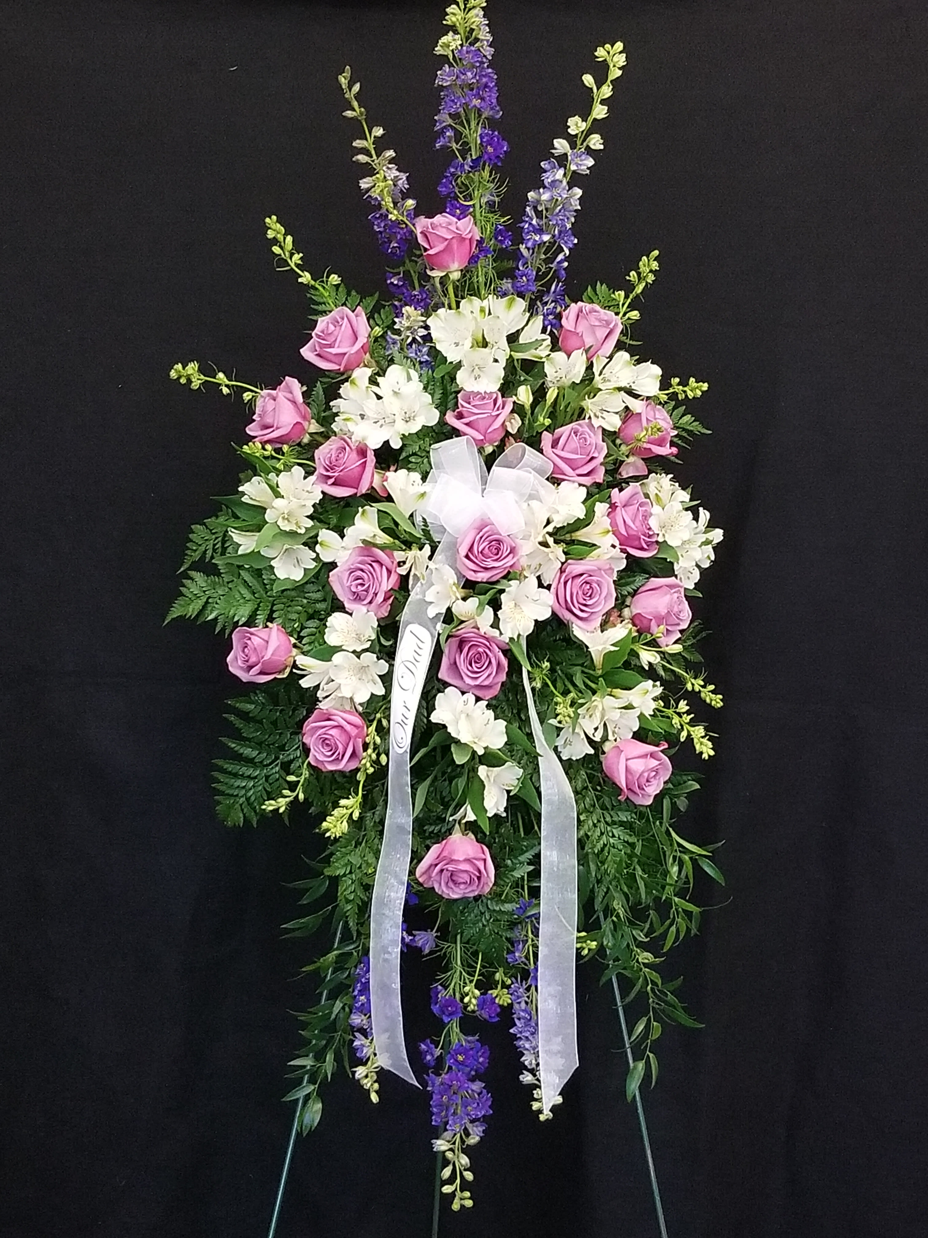 Standing floral spray with pink roses, white blooms, and purple accents on a black background