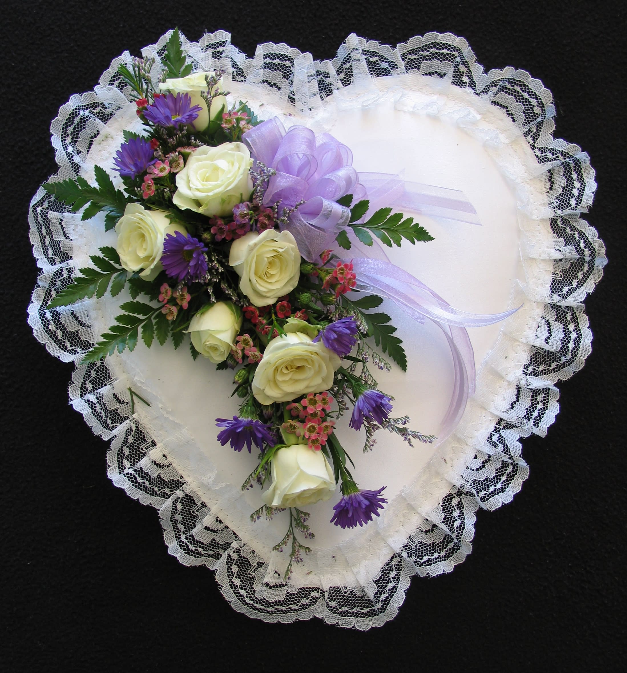 Heart-shaped lace pillow with a floral spray of white roses and purple flowers
