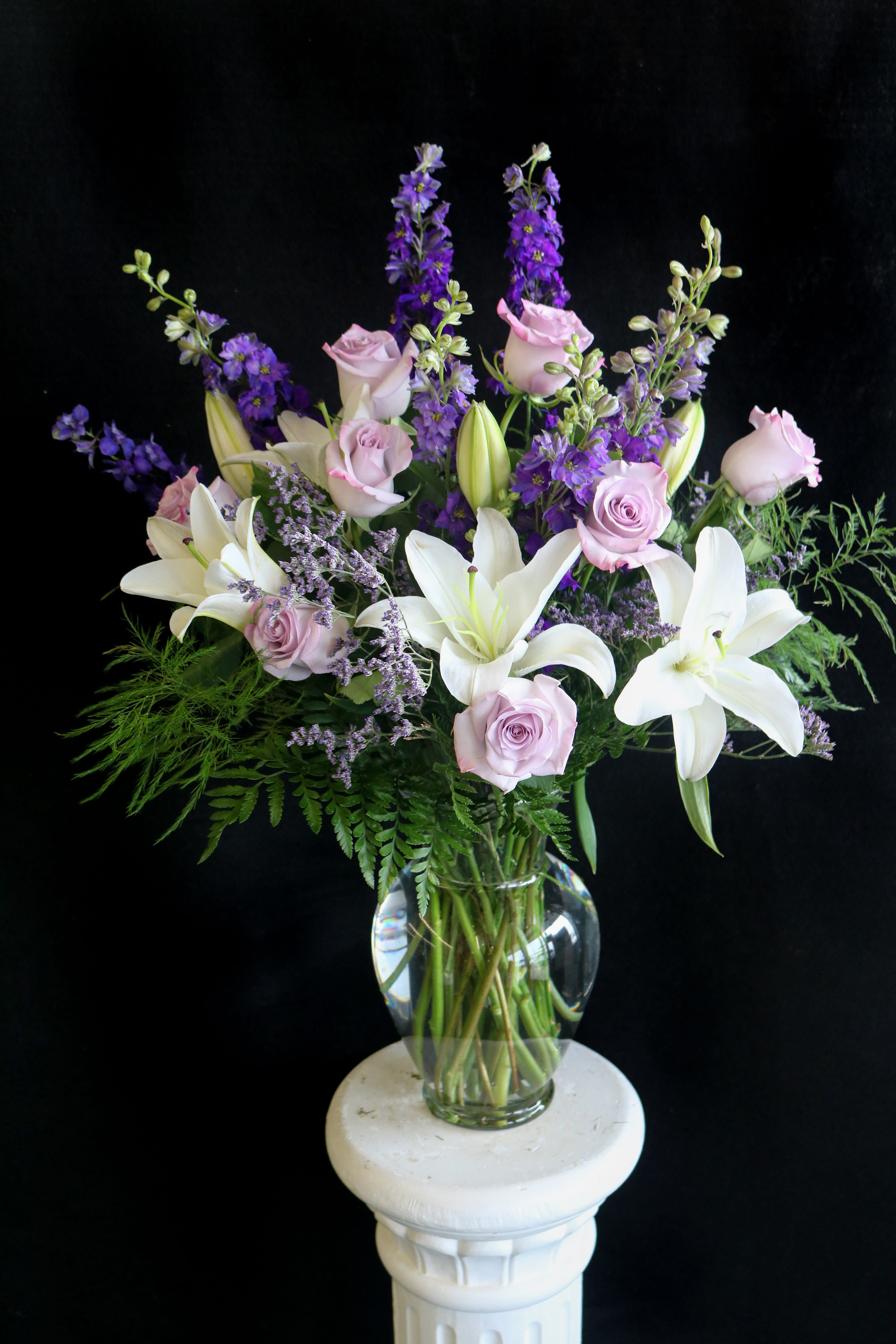 Bouquet of white lilies, pale pink roses, and purple flowers in a glass vase