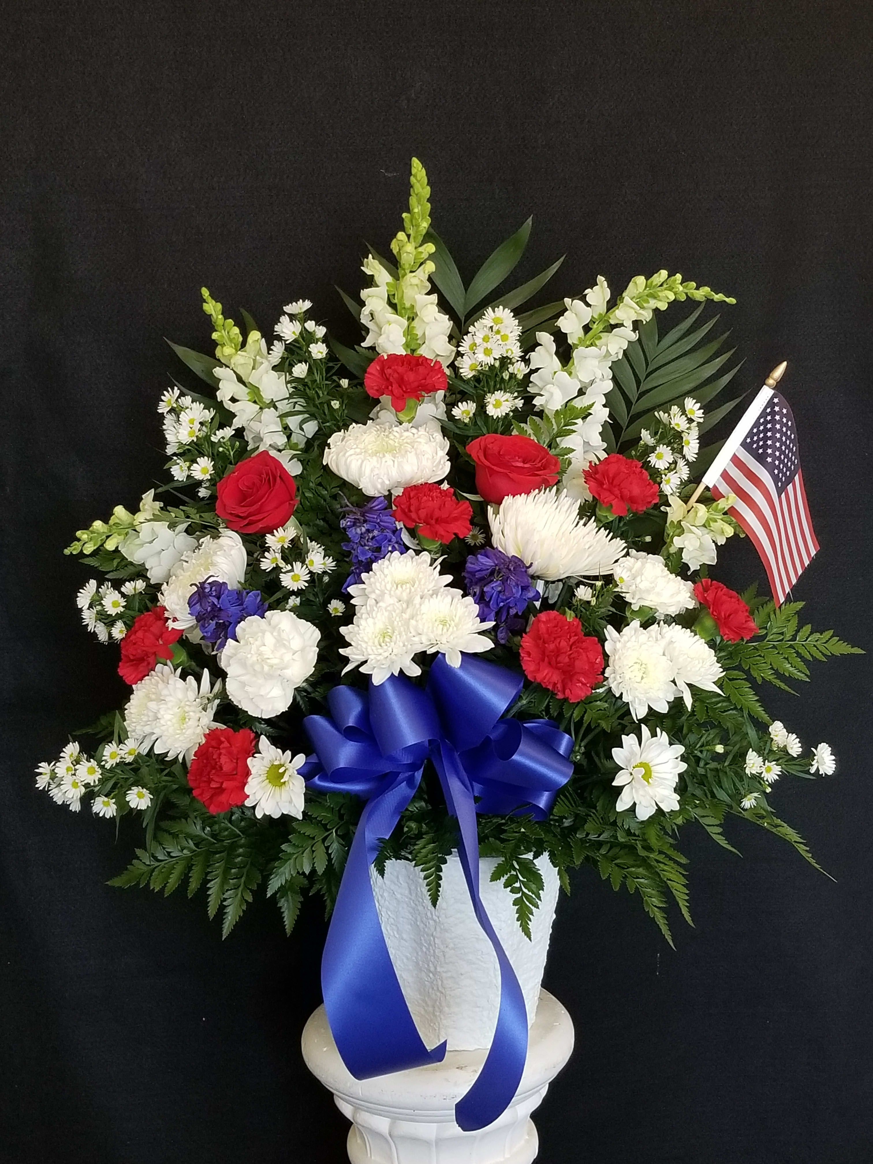 Red, white, and blue floral arrangement in a white vase with an American flag