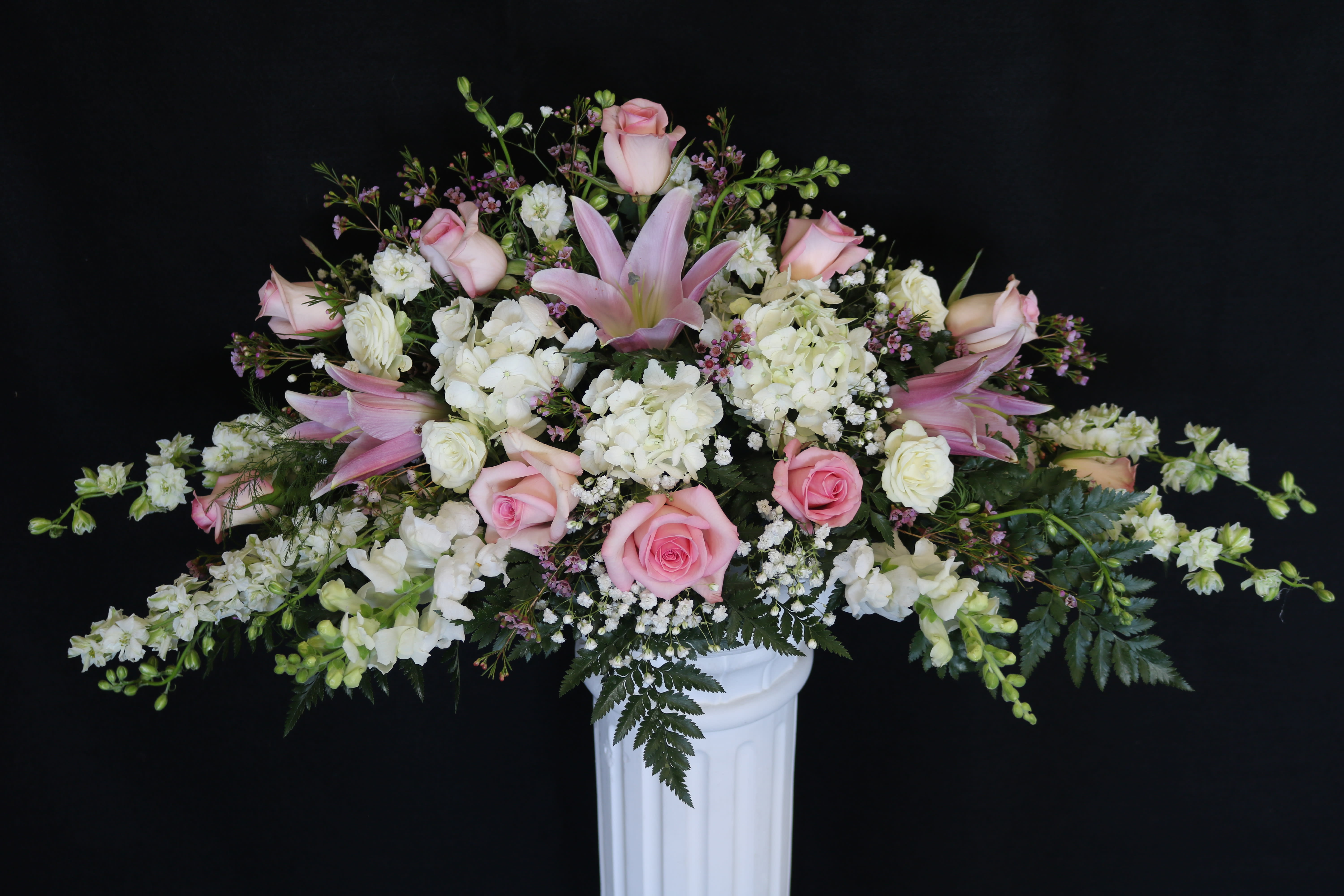 Pink roses and white flowers arranged in a white pedestal vase