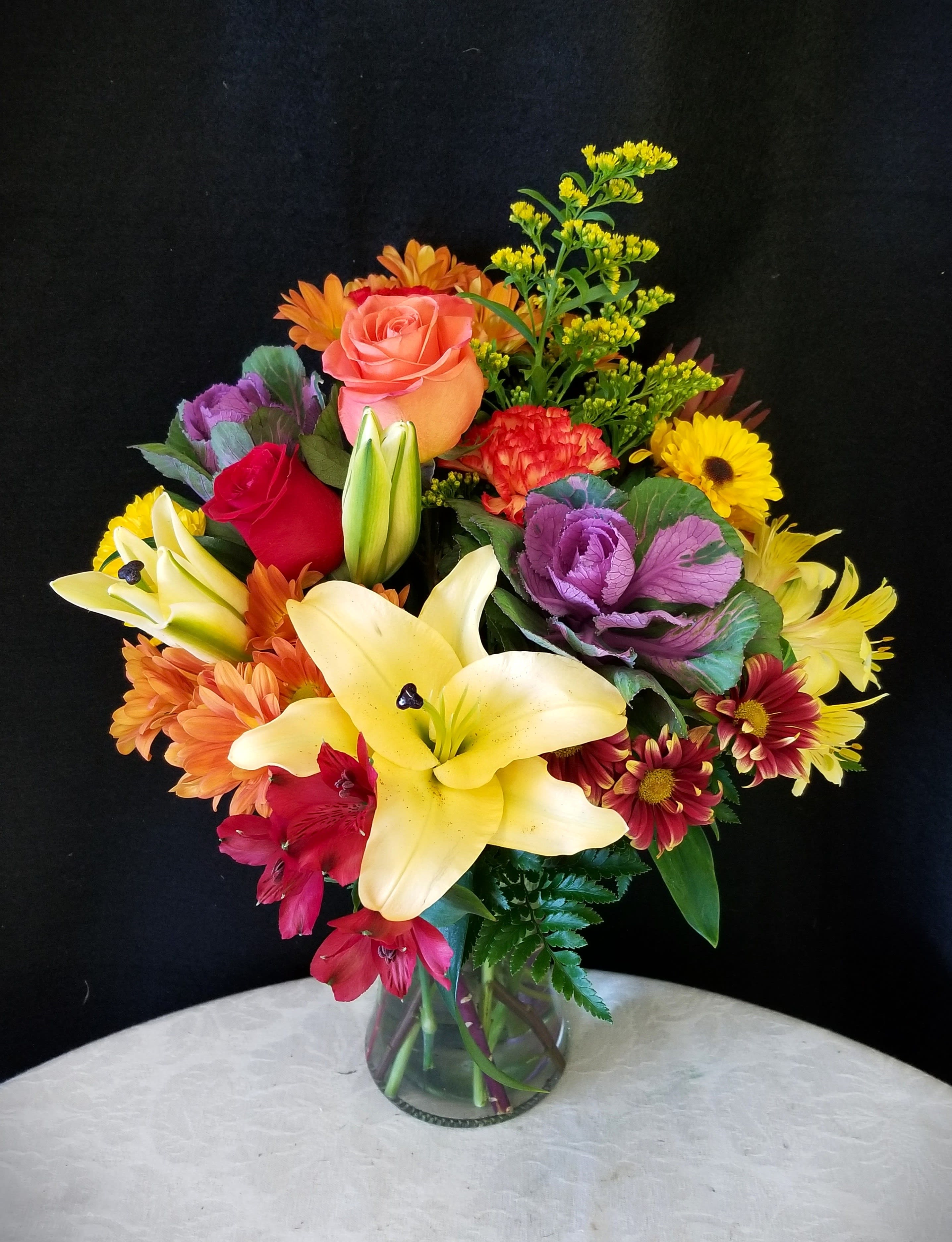 Mixed bouquet with lilies, roses, and daisies in a glass vase
