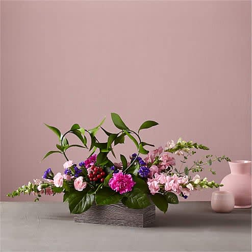Wild Romance Bouquet - Our Wild Romance Bouquet is a wonderful way to celebrate whatever stage of growth your relationship is flourishing in. The stand–out purple statice and pink carnations add bright balance to the assorted greenery fashioned into a heart, making it a statement centerpiece that celebrates love in every form.