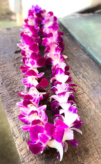 Two purple and white orchid leis laid on a wooden surface.