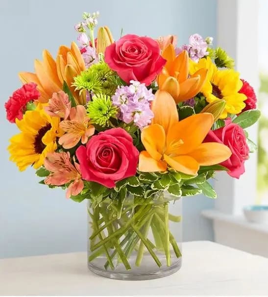 Bright mixed bouquet of roses, lilies, and sunflowers in a glass vase