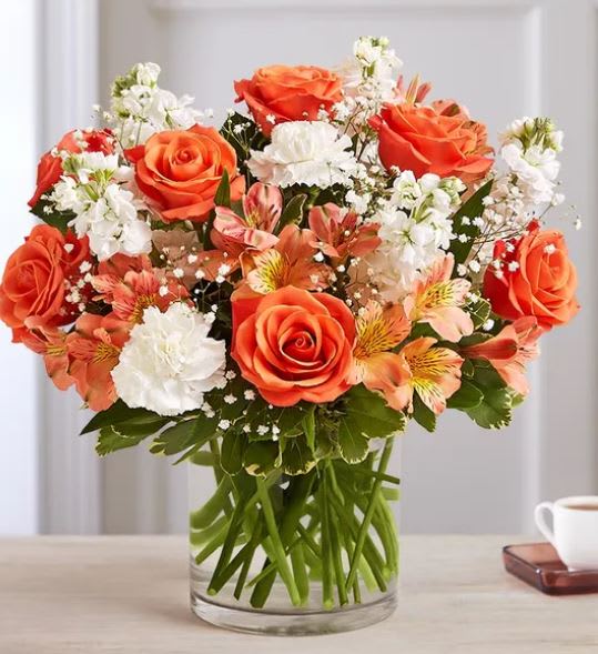 Orange roses and white flowers arranged in a clear glass vase