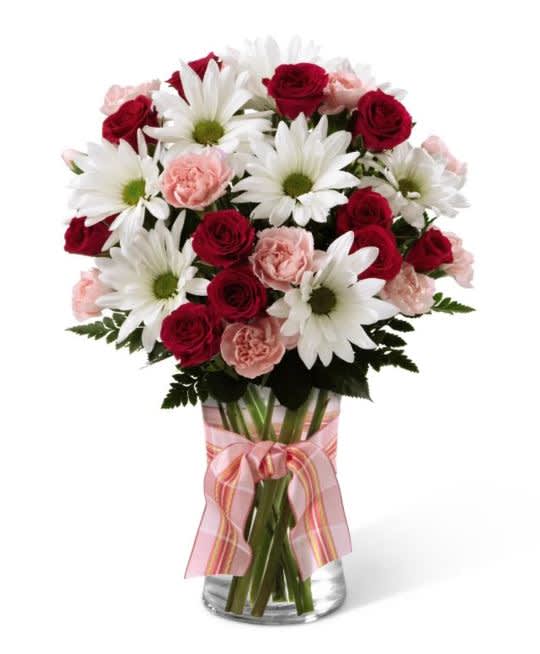 Sweet Surprise Bouquet - The Sweet Surprises Bouquet is an absolutely charming way to send  your warmest sentiments. Deep fuchsia and pink mini carnations, pink  roses, white traditional daisies and lush greens are sweetly situated, in  a classic clear glass vase accented with a perfectly pink designer.  ribbon to create a bouquet that will delight your special recipient at  every turn (Standard version does not include roses). Deluxe bouquet is shown. Premium has more flowers.  
