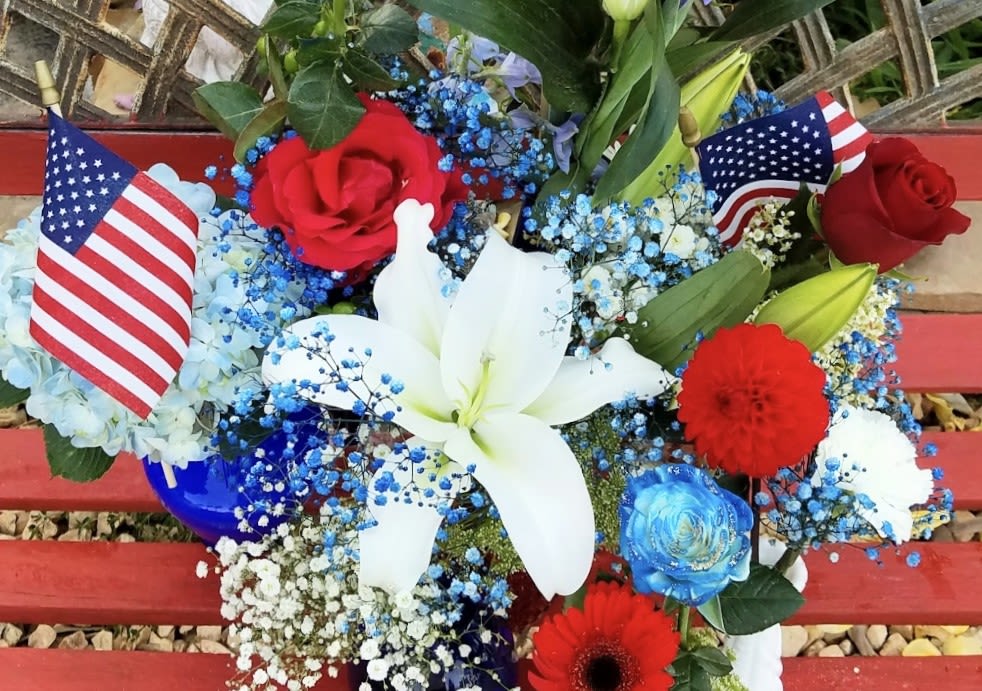Red, white, and blue floral arrangement with lilies, roses, and small flags