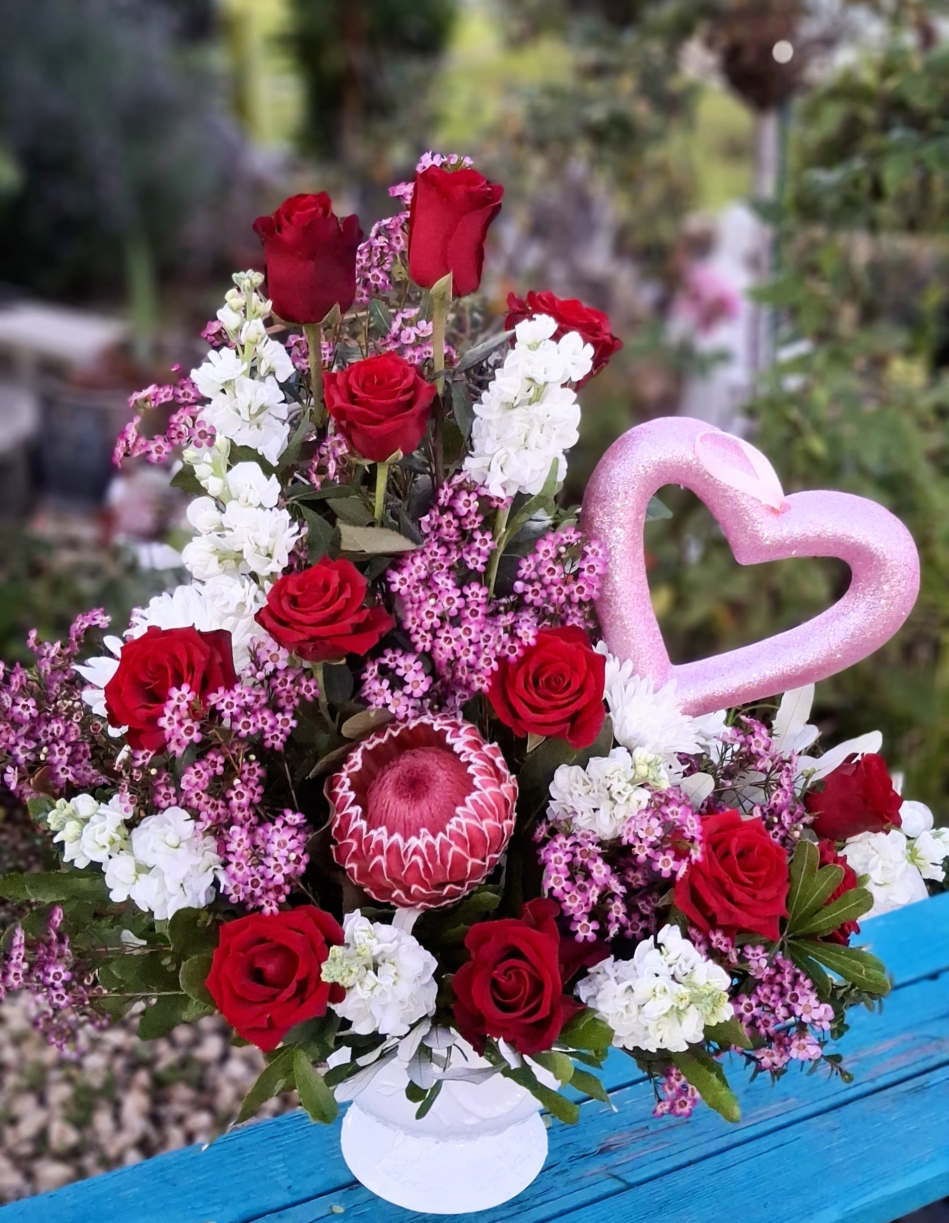 Red roses and white blooms in a vase with a pink heart pick