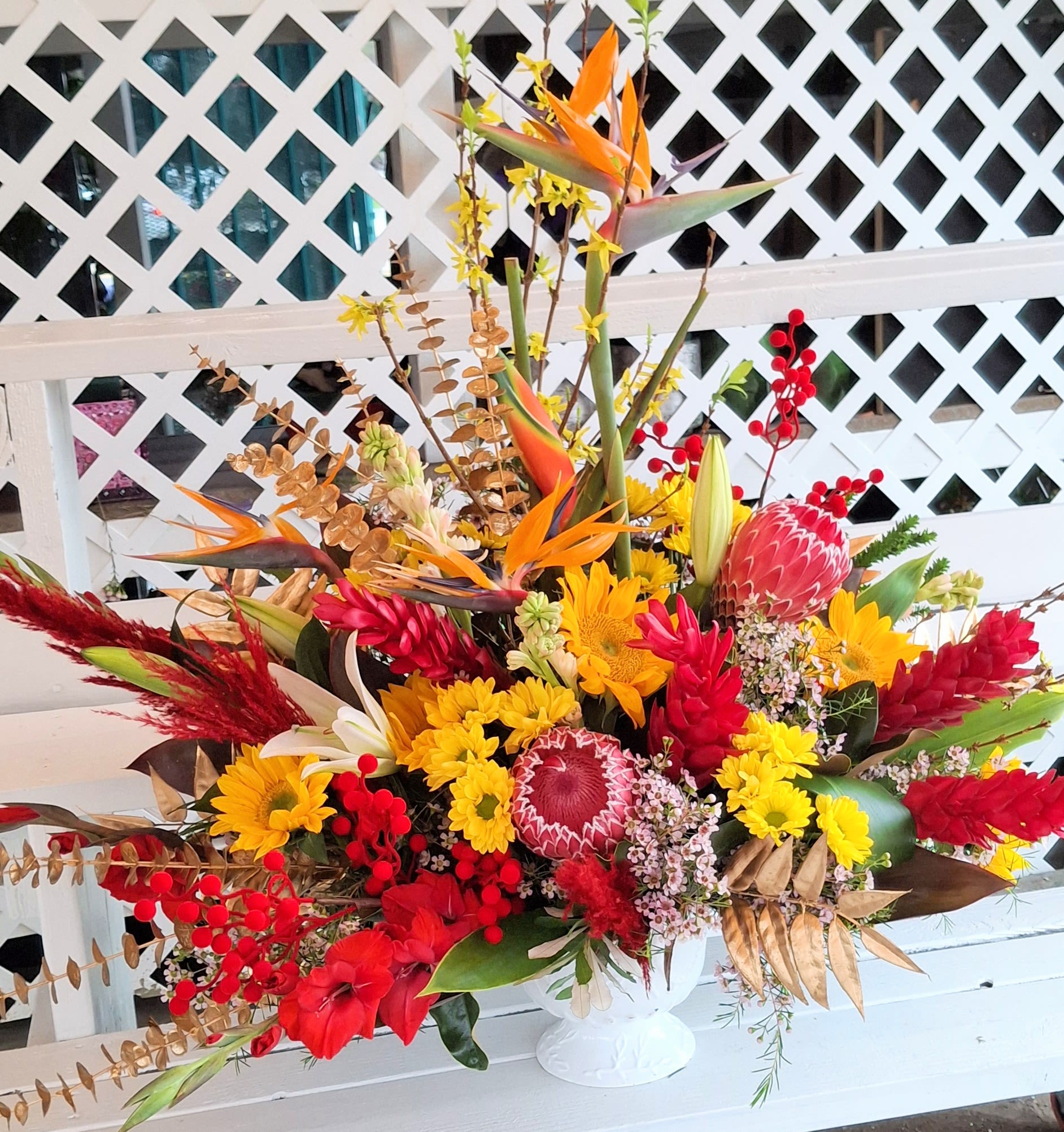 Large tropical bouquet with red, yellow, and orange flowers in a white vase