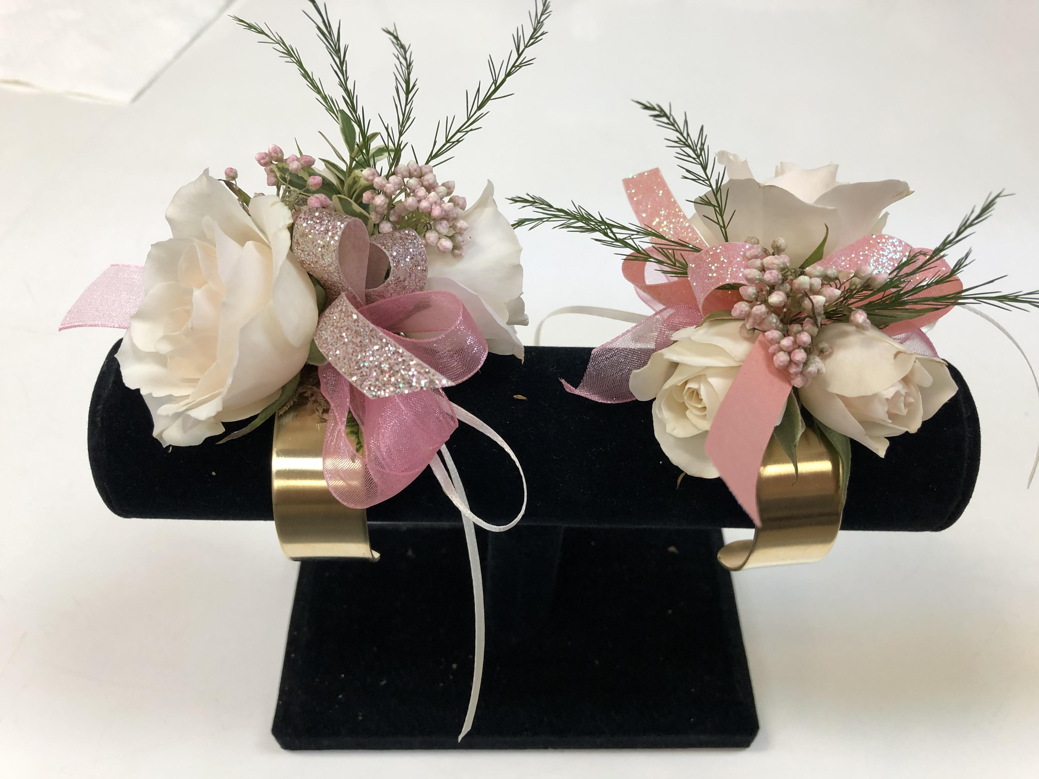 Pair of white floral corsages with pink ribbons on a black display stand