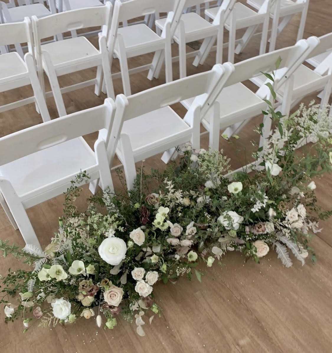 Low floral arrangement beside rows of white chairs