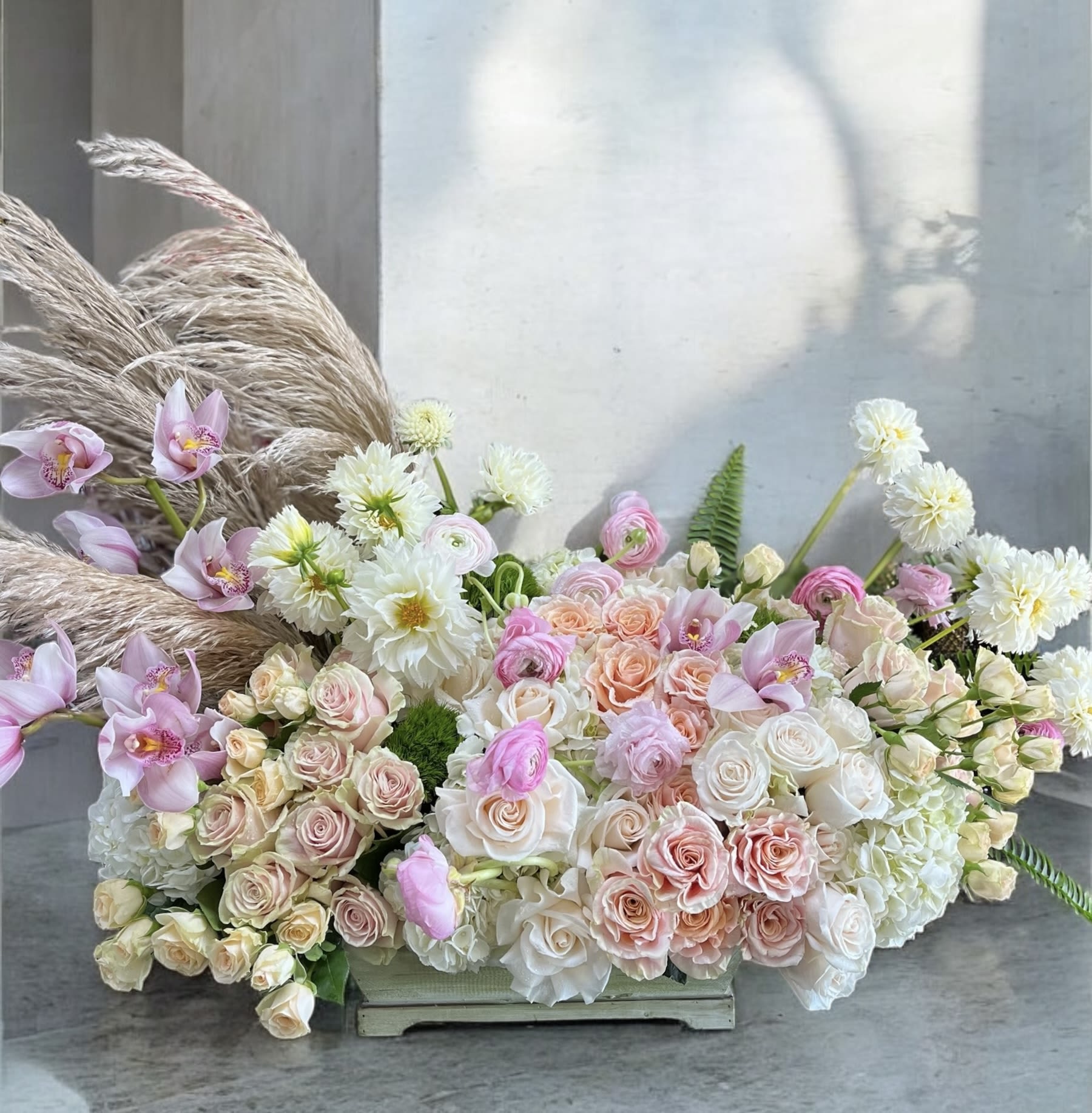Large pastel floral arrangement with roses, orchids, and white blooms in a low container