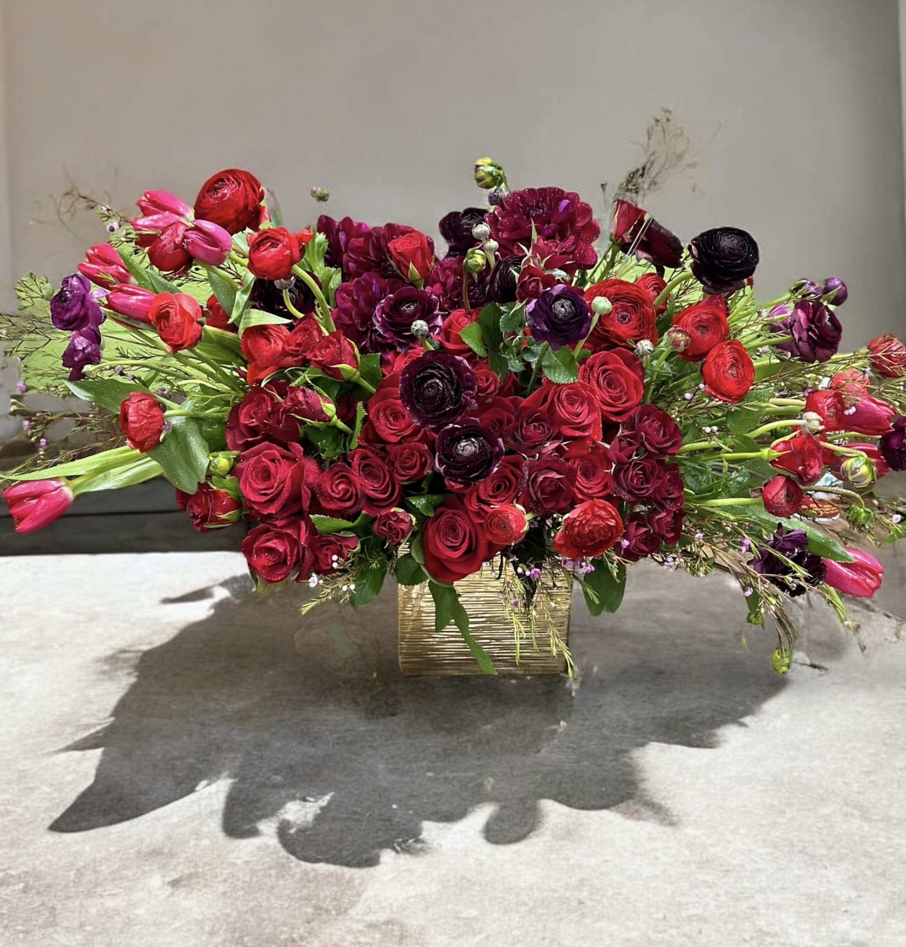 Large red and burgundy floral arrangement in a gold rectangular vase