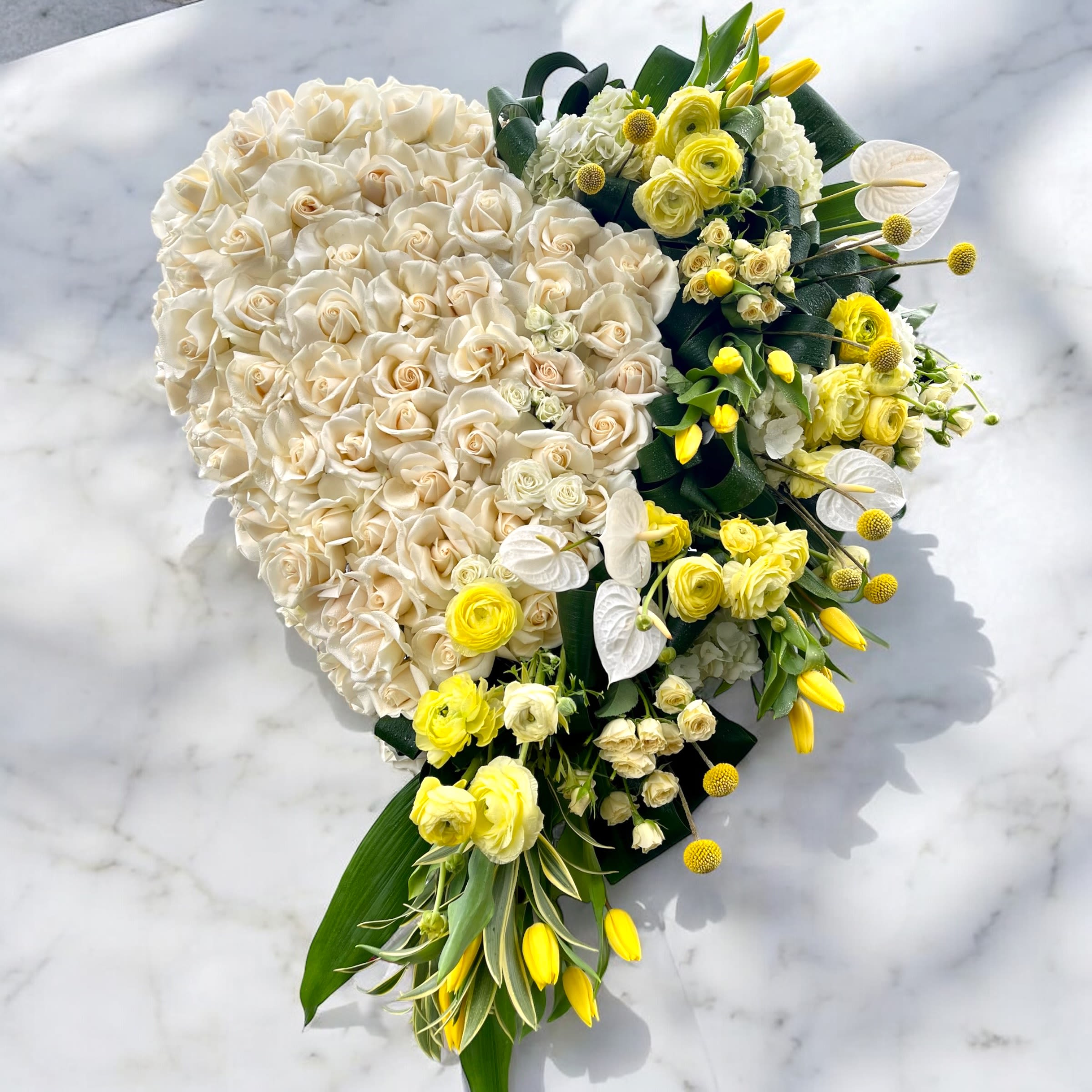 Heart-shaped bouquet of cream and yellow flowers on a marble surface