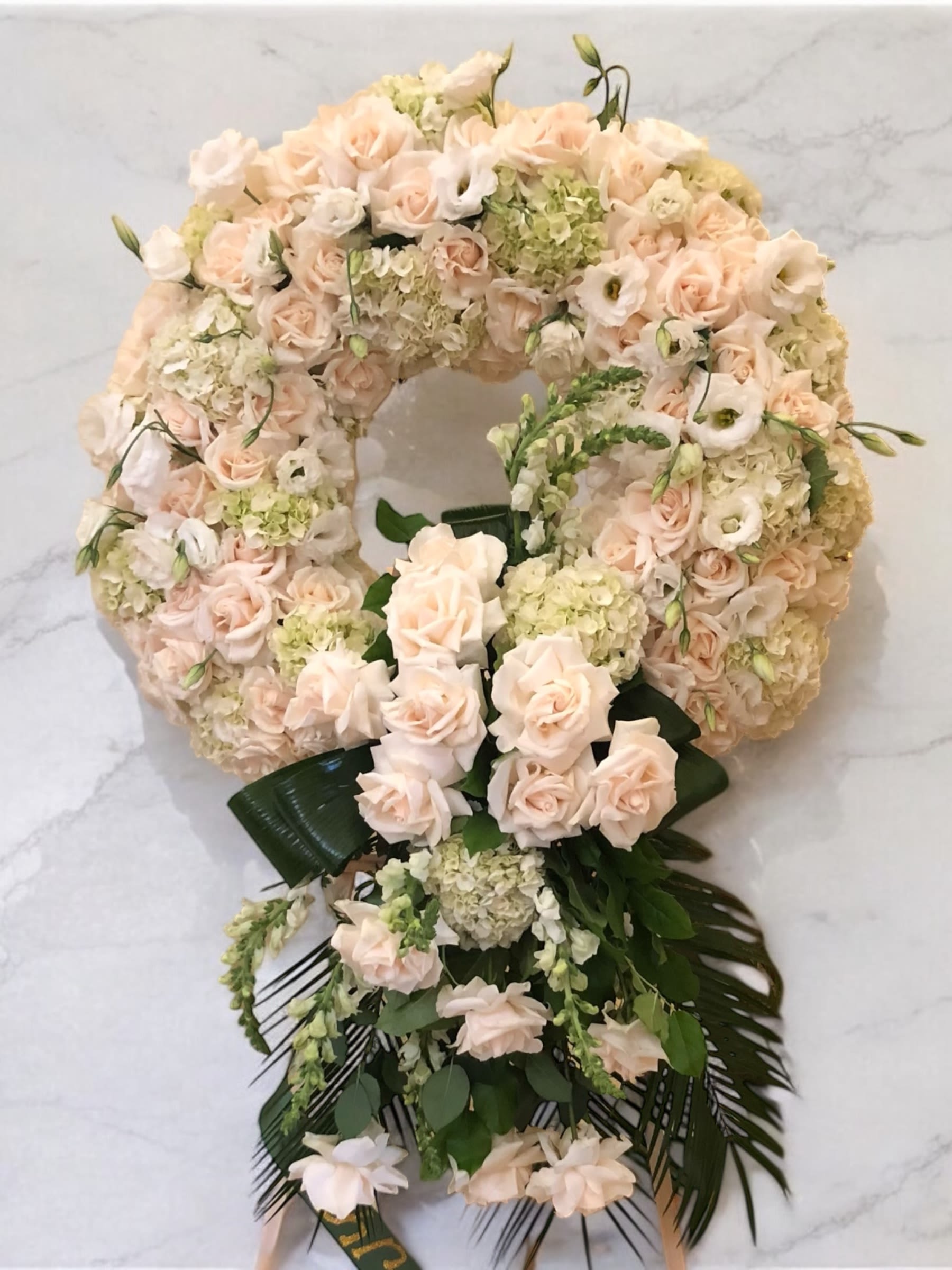 Large floral wreath of pale pink roses and cream blooms with dark green ribbon