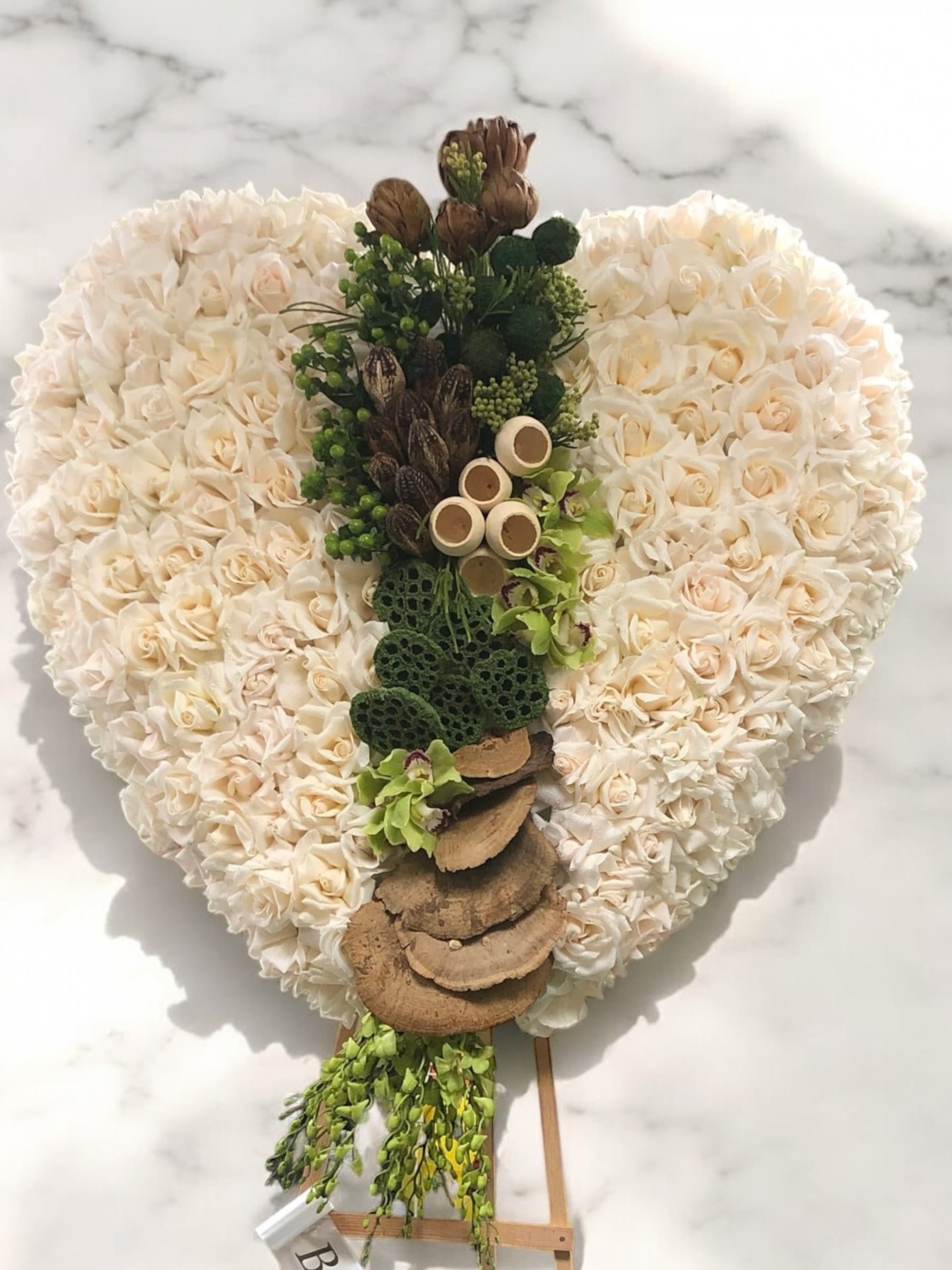 Heart-shaped floral arrangement of cream roses with a central green-and-brown decorative cascade